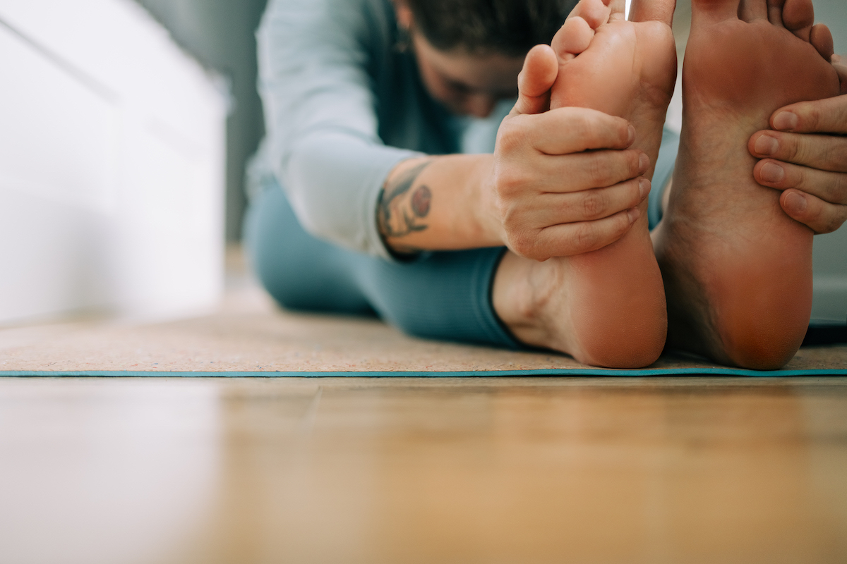 Nő kék jógaruhában, tetoválással a kezén, lábujjérintés közben