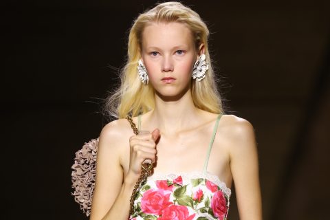 Egy virágmintás ruhát viselő modell sétál komoly arccal a kifutón