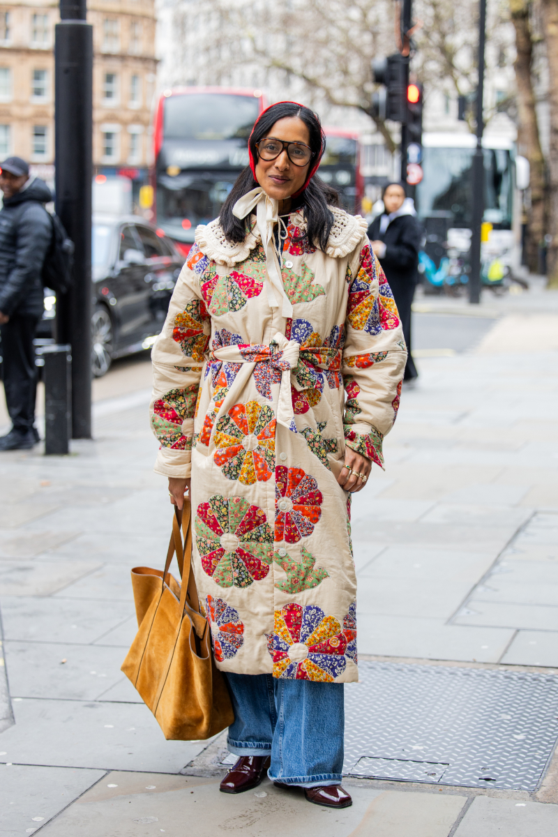 Egy vendég piros fejkendőben és mintás, övvel megkötött bézs kabátban a Paul Costelloe-bemutató előtt a 2026-os őszi–téli londoni divathéten.