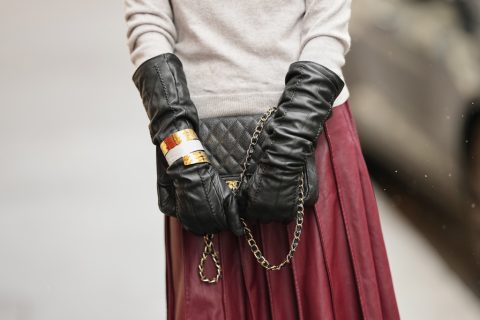 Egy fehér pulóveres nő bőrkesztyűt visel, kezei között fekete táska