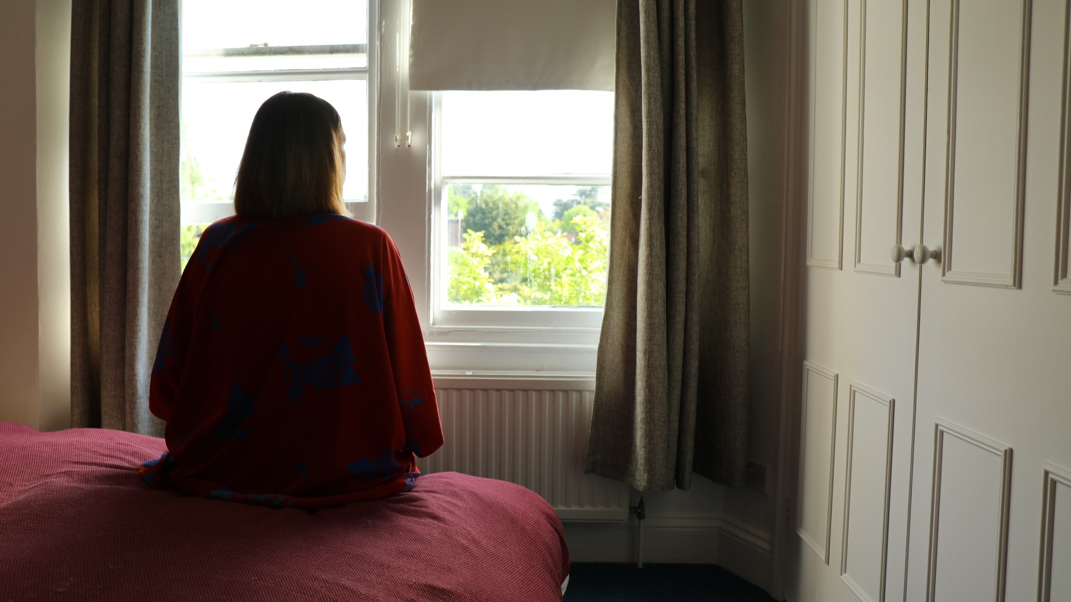 Egy nő ül a hálószobában néz ki az ablakon