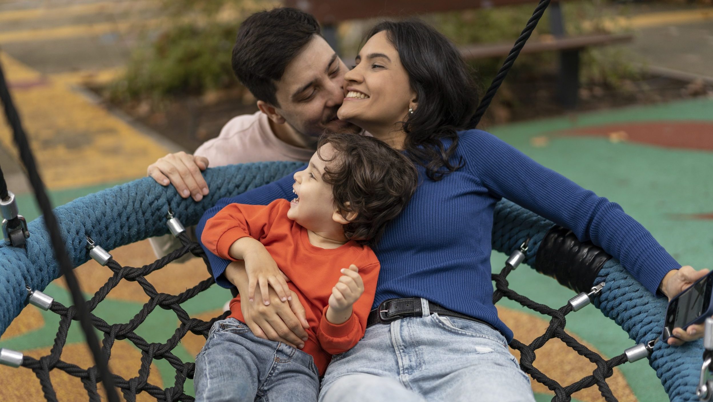 Kisgyerek és anyuka hintázik és egy férfi megcsókolja az anyukát