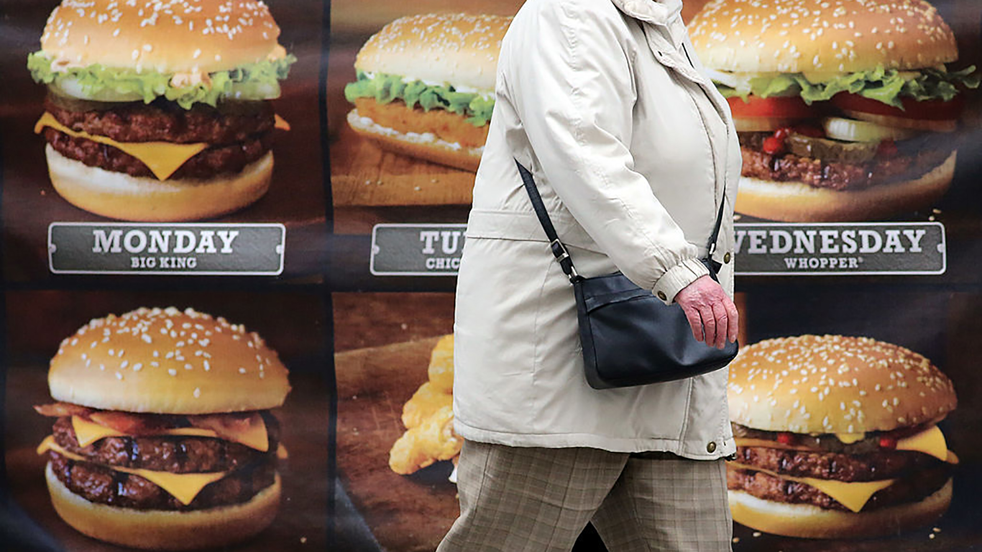 Túlsúlyos személy hamburger reklámok előtt sétál el