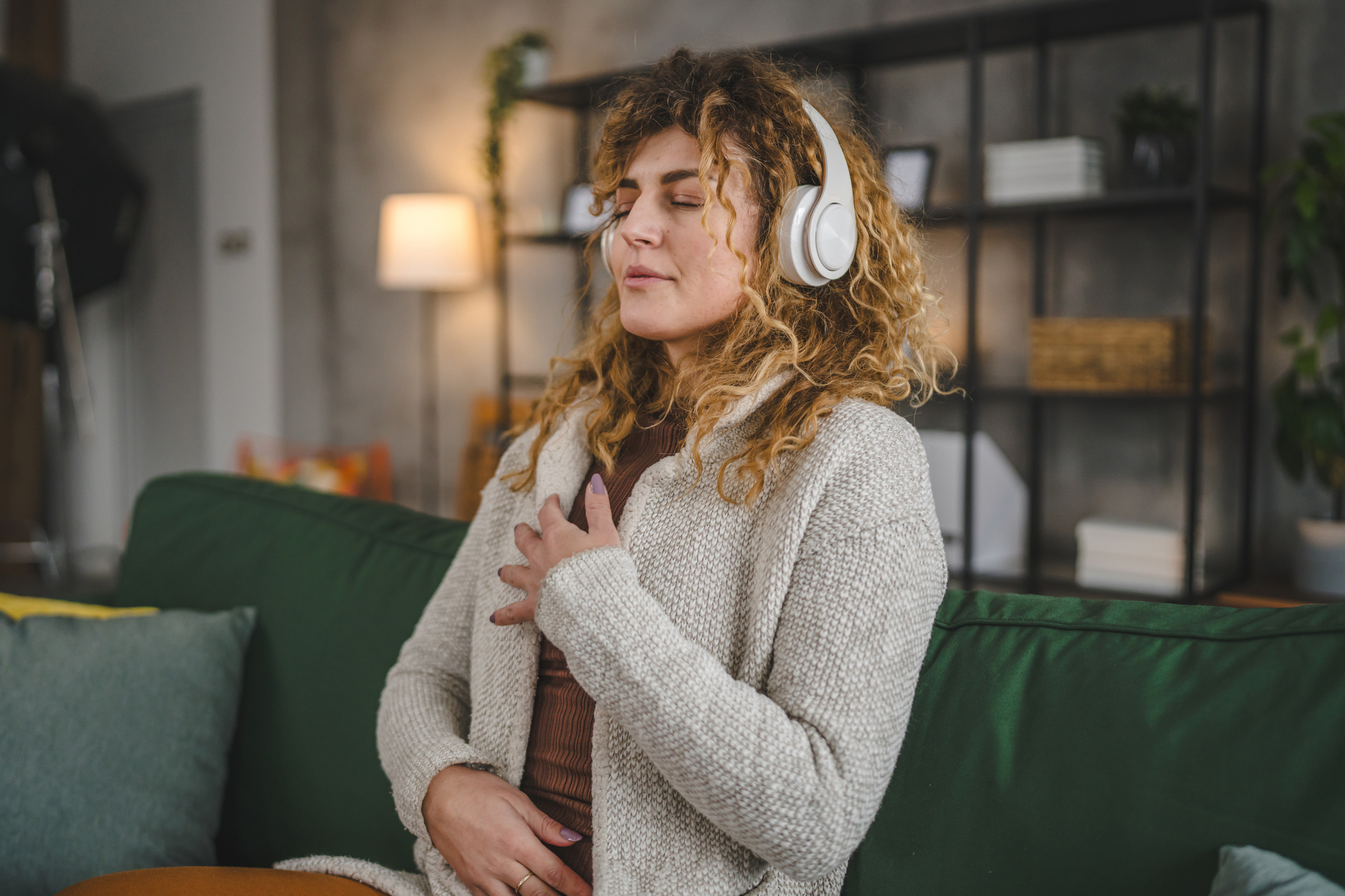 nő fehér fülhallgatóval, mellkasára tett kézzel, lehunyt szemmel