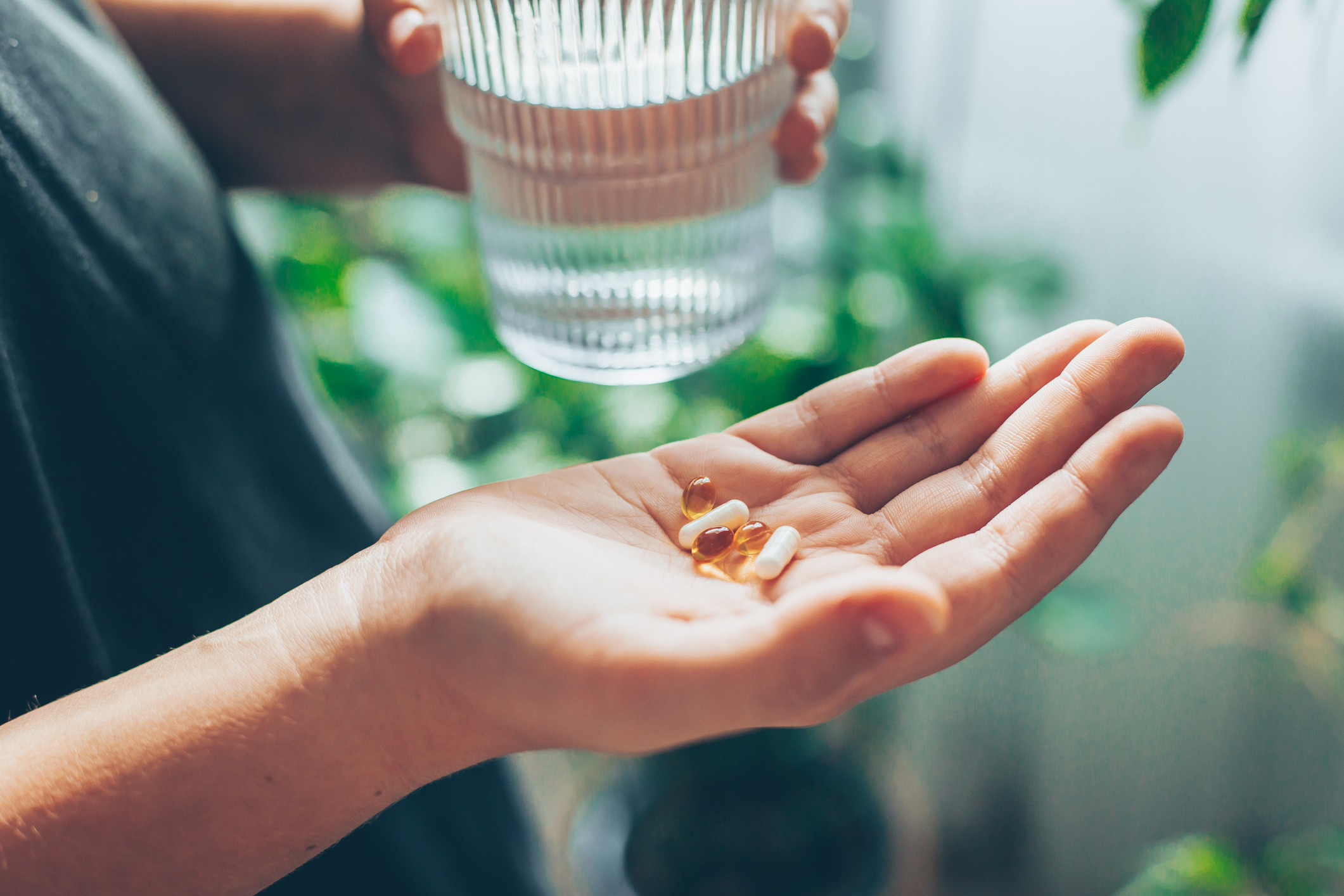 Nő, aki vitaminokat, tablettákat vagy kapszulákat tart a kezében, és egy pohár vizet. Wellness, jólét koncepció