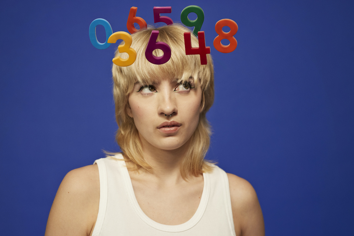 fiatal nő szőke hajjal, mögötte kék háttér, a feje felett színes számok lebegnek