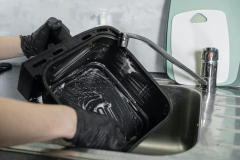 fekete kesztyűs kéz csap alatt elmos egy habos air fryer kosarat