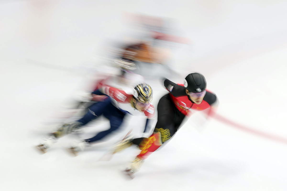 gyorskorcsolyázó fehér háttér előtt megelőzi a többi versenyzőt