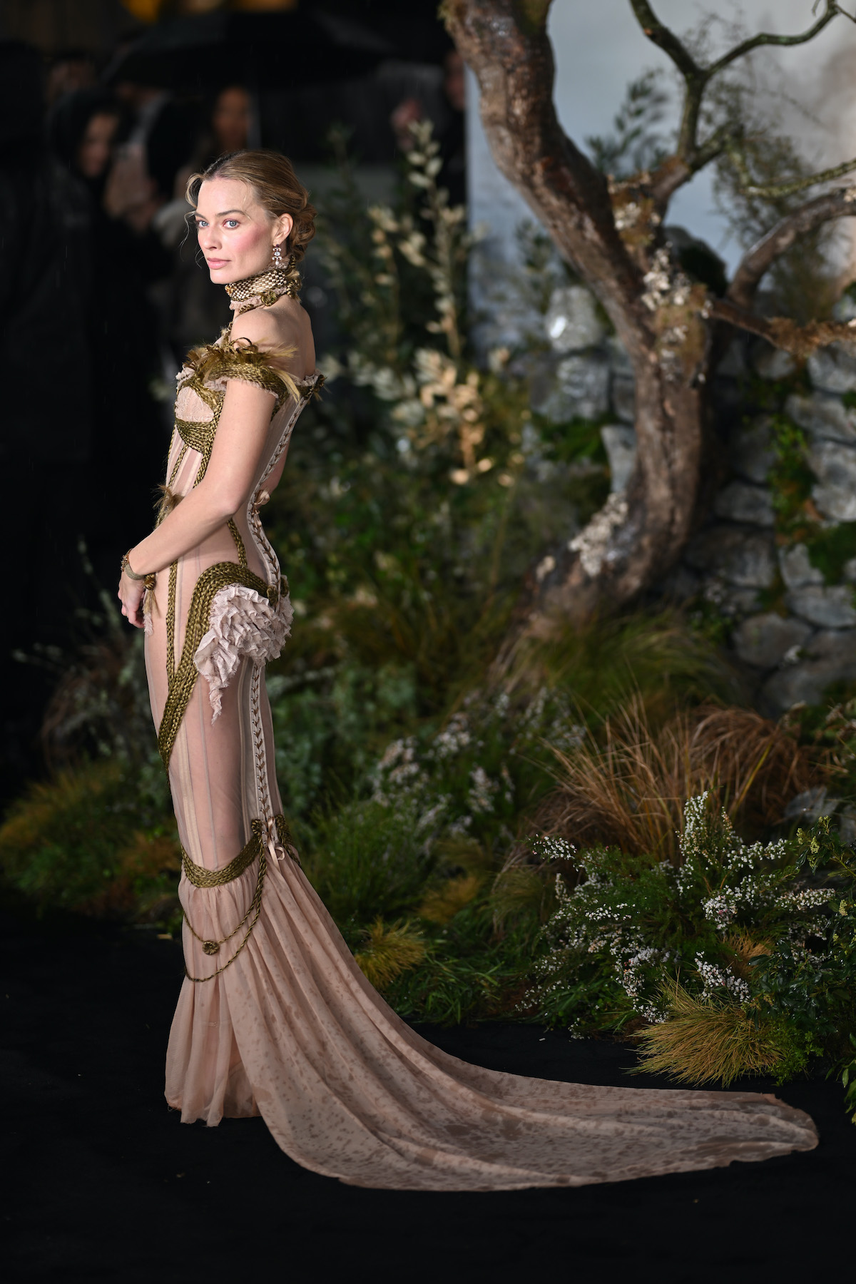 szőke nő földig érő ruhában: hátán a gerinc vonalát fonott hajmintázat rajzolja ki, amely a deréknál szándékosan eldolgozatlan, rojtos textúrában végződik. 