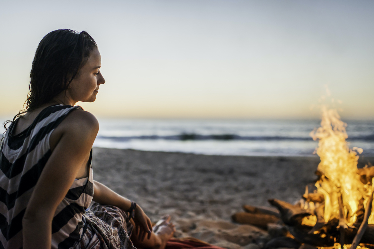 Fiatal nő tűznél ül tengerparton