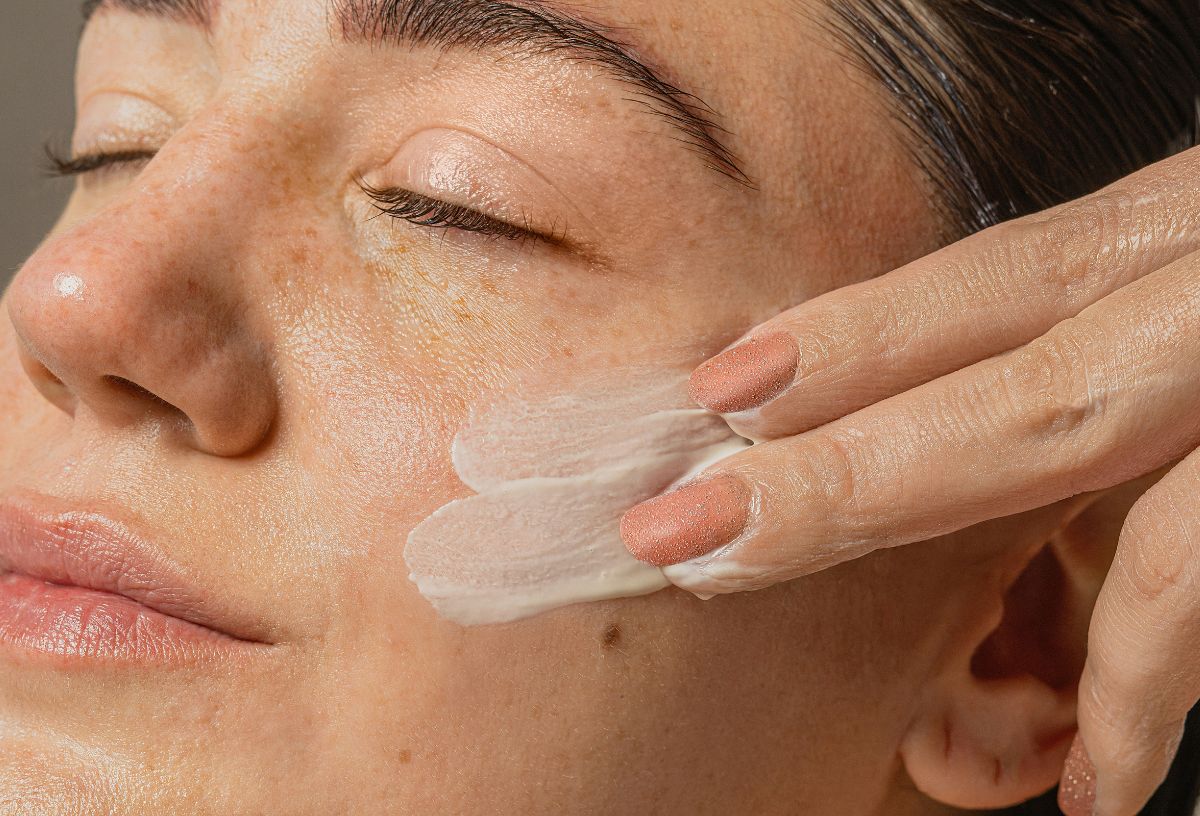 Nő csukott szemmel krémet ken az arcára a szeme alatt két ujjal