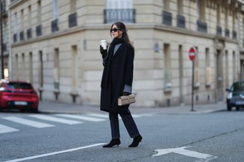 Bianca Derhy hosszú, sötétbarna haját középen elválasztva, lazán a vállára omlatva viseli. Sminkje természetes hatású, egységes arcbőrrel és visszafogott, neutrális rózsaszín rúzzsal. Fekete, oversized gyapjúkabátot visel hajtókás gallérral és egyenes szabásvonallal, alatta sötétkék kötött pulóverrel rétegezve. Nadrágja sötétkék, egyenes szárú, kissé rövidített fazonú farmer. Ehhez fekete velúr, hegyes orrú bokacsizmát választott alacsony kitten sarokkal. A szettet fekete gyapjúsál egészíti ki a nyaka köré tekerve, barna kesztyű, fekete Celine napszemüveg, valamint egy világos bézs, téglalap alakú, felső füllel ellátott bőrtáska a Savette-től. A kezében egy fehér elviteles kávéspoharat tart, egy street style divatfotózás során.