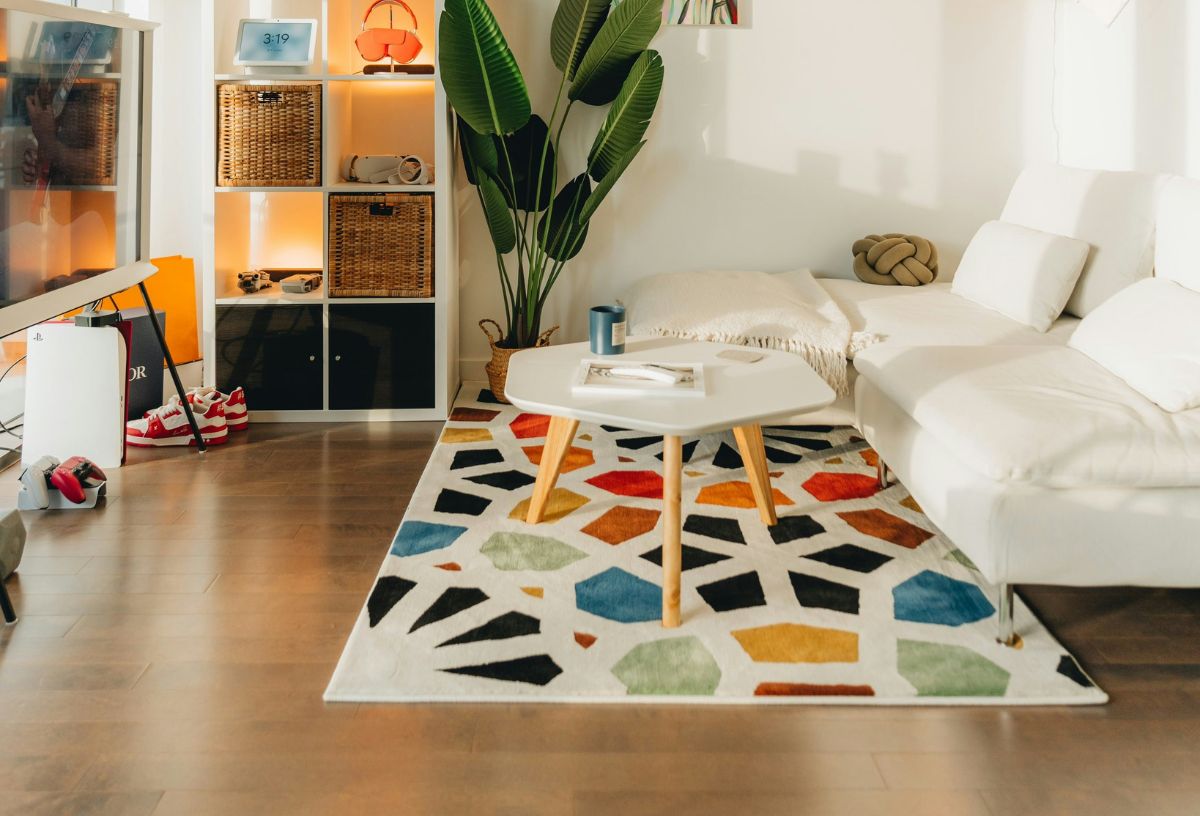 Színes szőnyeg nappali szobában, rajta három lábú kávézóasztal, fehér kanapé, mögötte zöld nagylevelű szobanövény