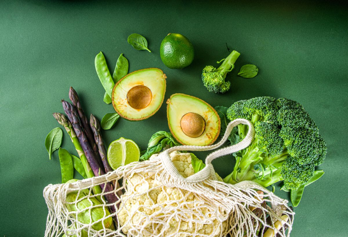 Zöld háttéren zöld színű zöldségek és gyümölcsök hálós bevásárlószatyorból gurulnak ki