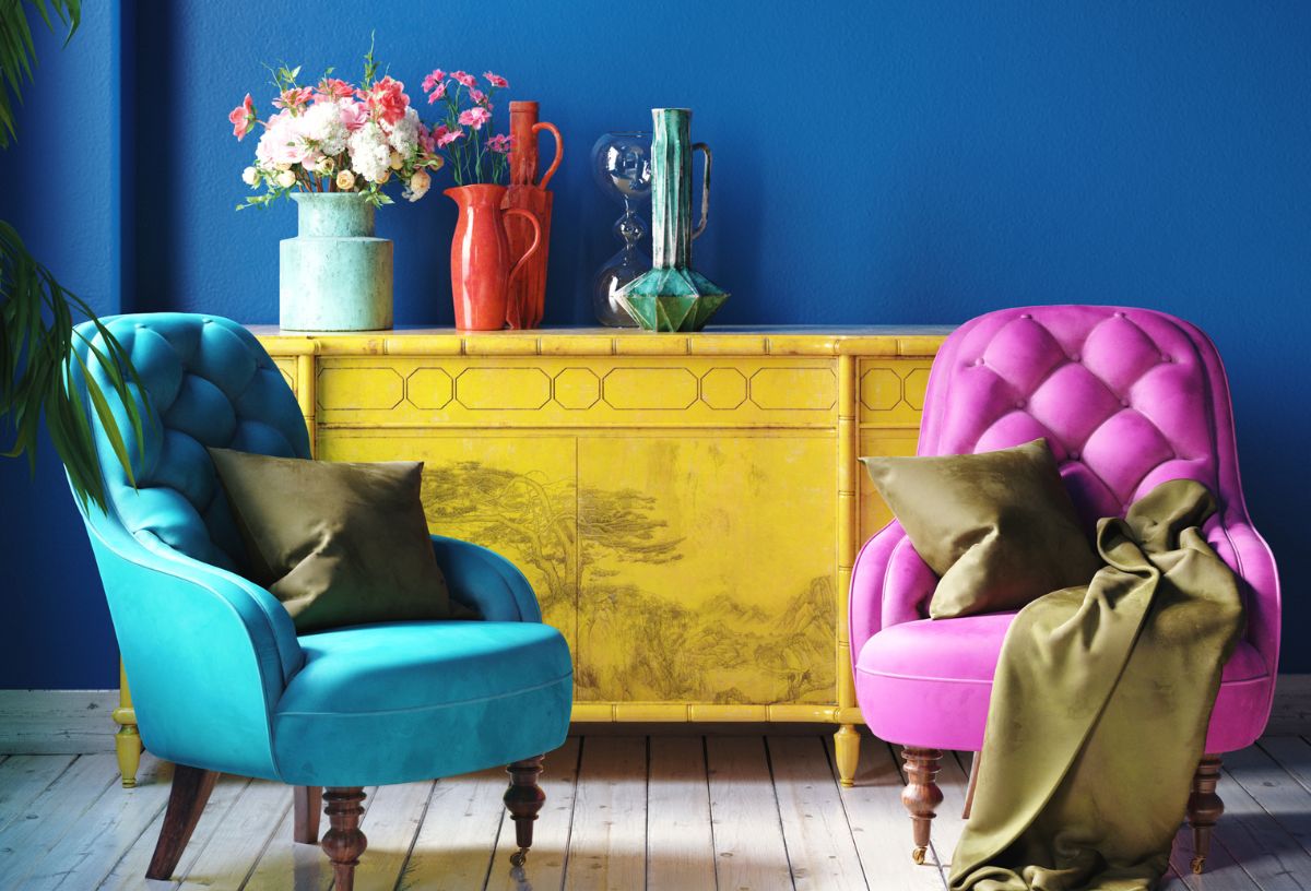 Retró hatású, erős színekkel berendezett nappali, kék és rózsazsín fotel, olajzöld díszpárnák, kék fal, sárga komód színes vázákkal