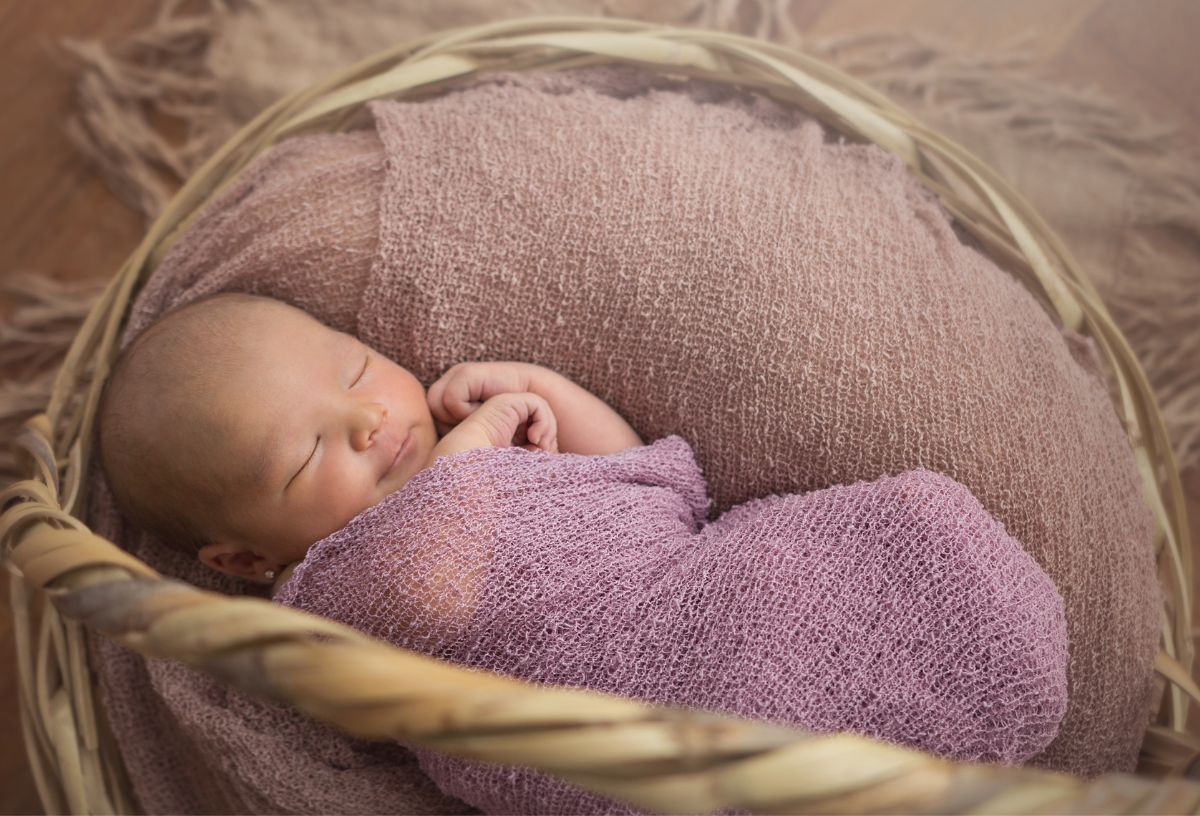 Lány kisbaba fáradt rózsaszín kötött pólyába takarva mályvaszínű anyaggal kibélelt kosárban alszik