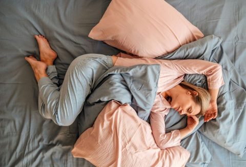 Szőke nő rózsaszín-szürke pizsamában alszik rózsaszín-szürke ágyneműben