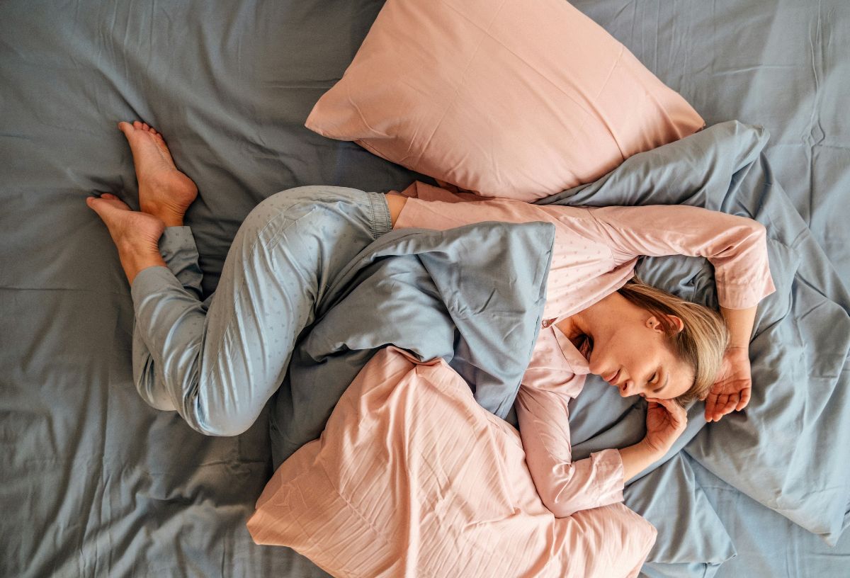 Szőke nő rózsaszín-szürke pizsamában alszik rózsaszín-szürke ágyneműben