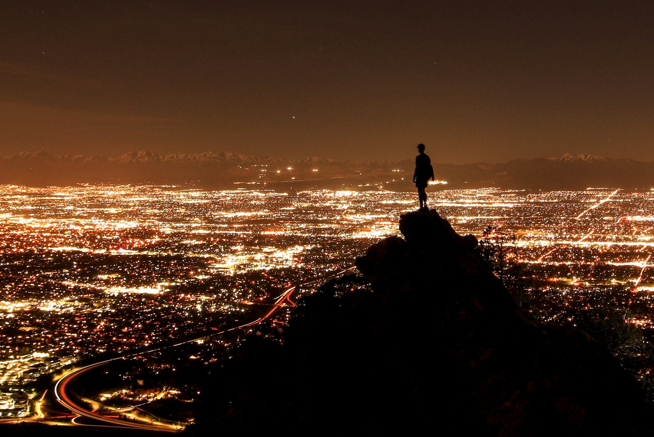 Egy ember a sziklán állva nézi at éjszaka kivilágított várost