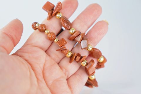 Egy női kéz két karkötöt tart a kezében, mindegyikben barna színű drágakövek láthatók