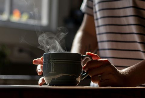 Nő reggeli fényekben kezében zöld csészét fog, amiben gőzölgő meleg víz van