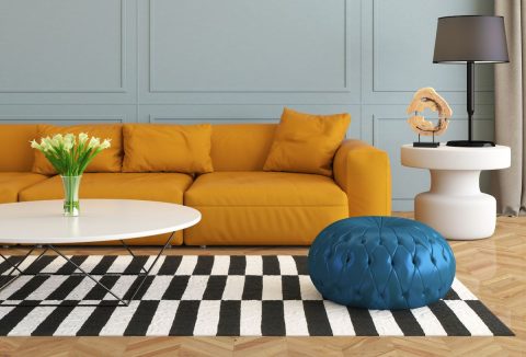 Modern nappali mustársárga kanapéval, kék ottománnal, fekete-fehér csíkos szőnyeggel