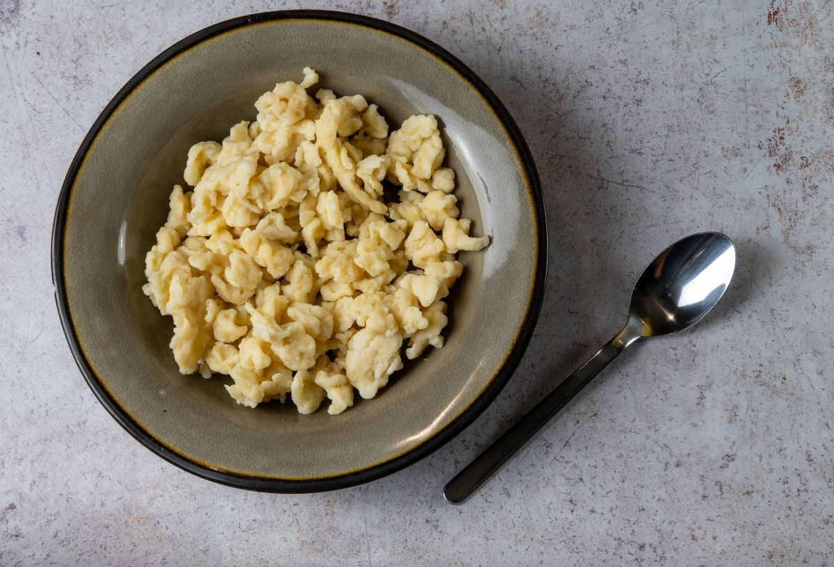 Nokedli kerámia tányéron szürke kőasztalon, mellette kanál