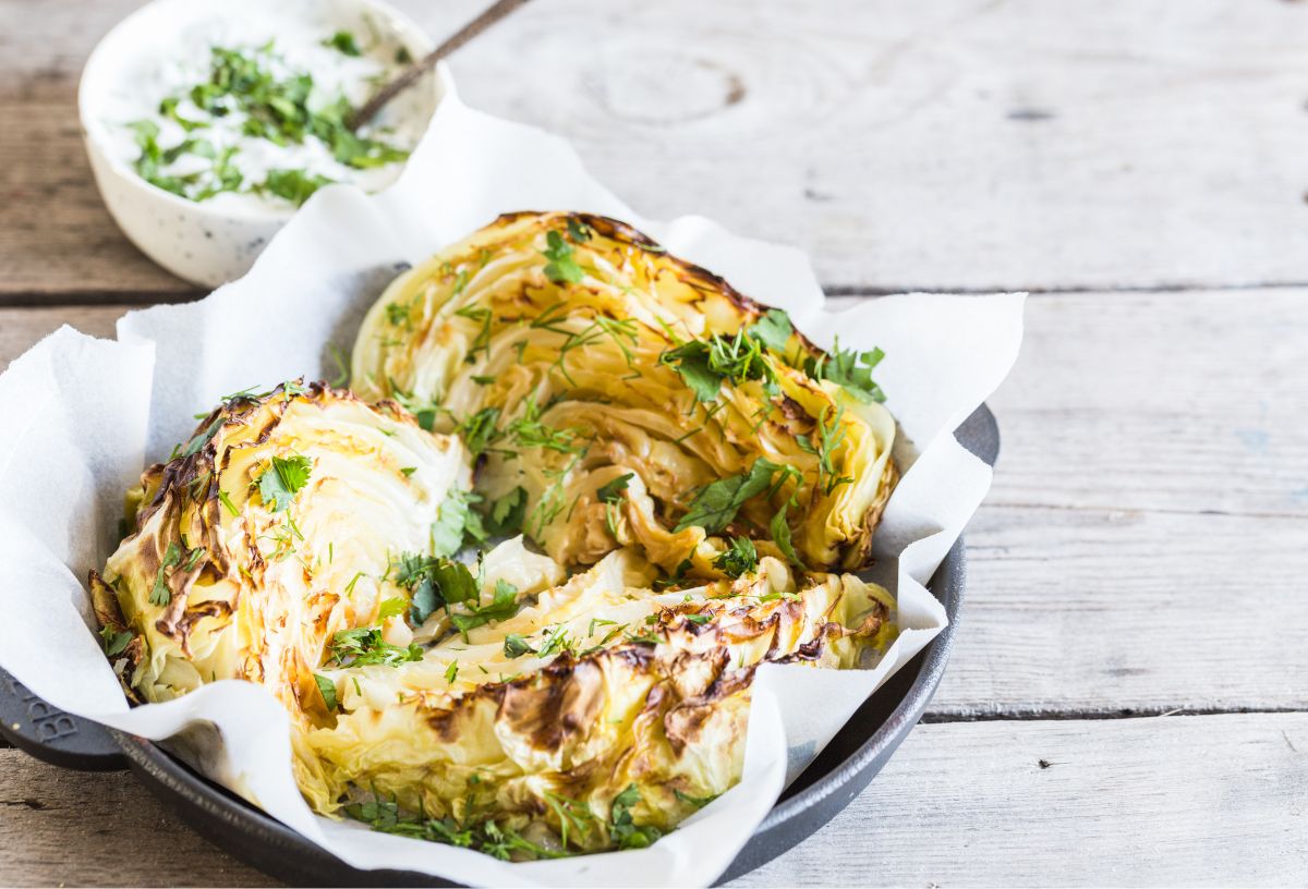 Olvadó káposzta serpenyőben, petrezselyemzölddel megszórva, háttérben tejfölös öntet