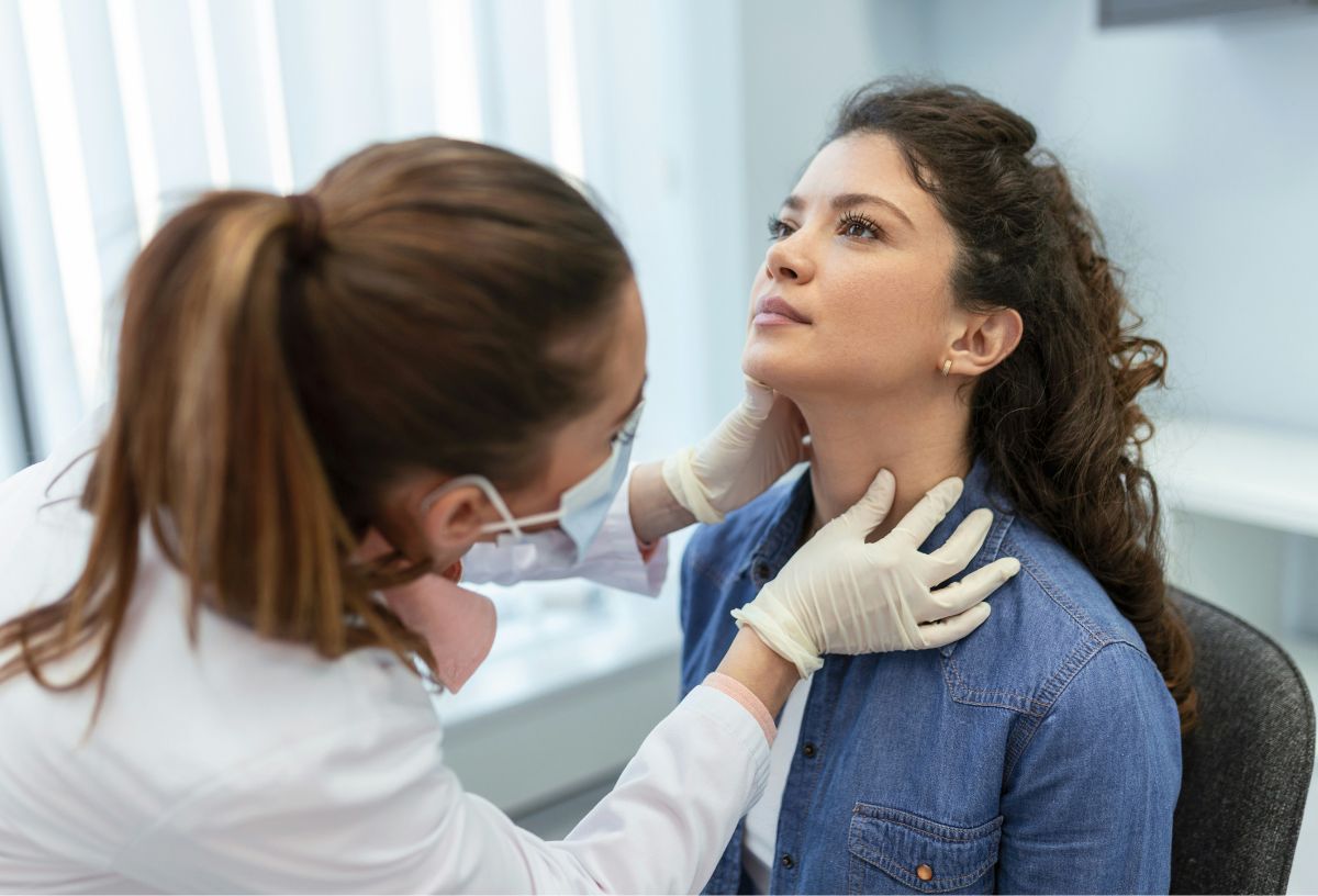 Endokrinológus orvos vizsgálja fiatal, göndör hajú nő nyakán tapintással a pajzsmirigyet