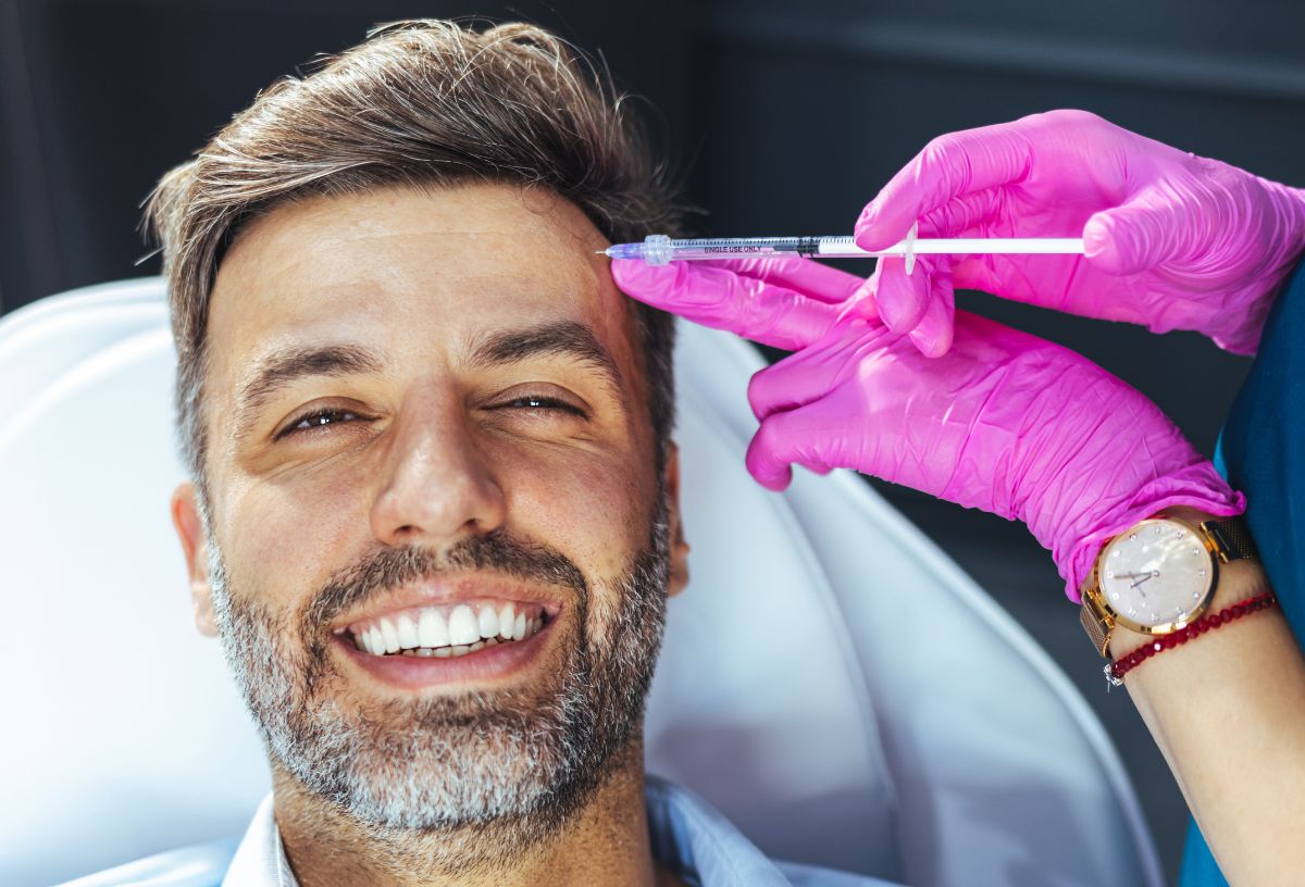 Mosolygó középkorú, őszülő szakállas férfi plasztikai sebésznél botoxinjekciót adat a homlokába