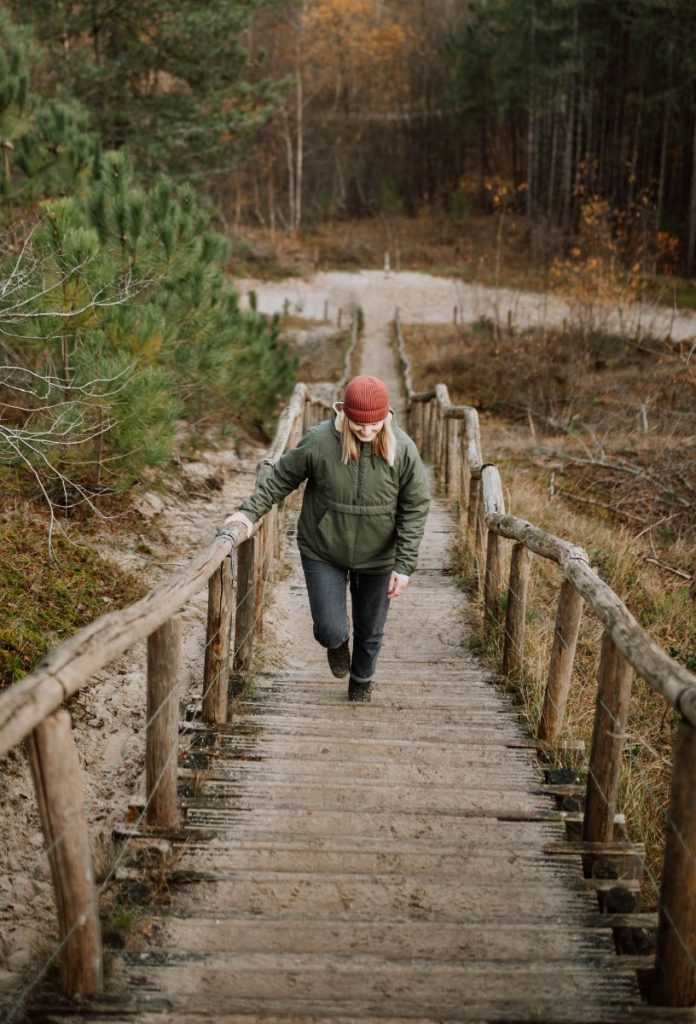 Nő téli ruházatban gyalogol fel lépcsőn parkerdőben