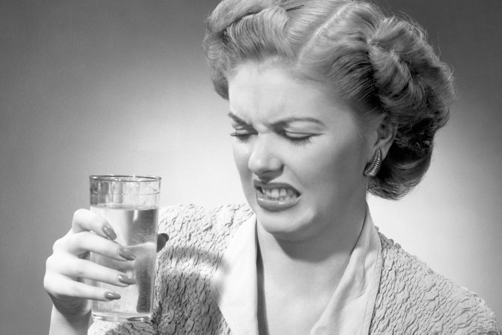 Egy nő az 1950-es években undorodva néz egy pohár vízre