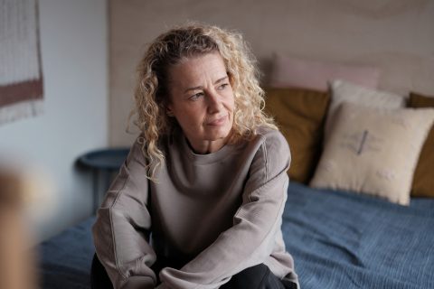 Egy 50 feletti nő szomorúan ül az ágyán a szobájában