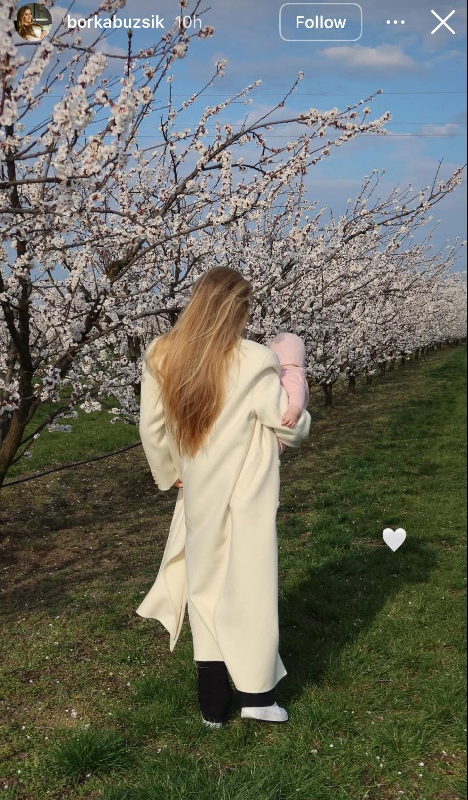 Szoboszlai Dominik felesége, Buzsik Borka fehér kabátban, háttal, és karjában lányuk a cseresznyevirágzást csodálják – Instagram sztori
