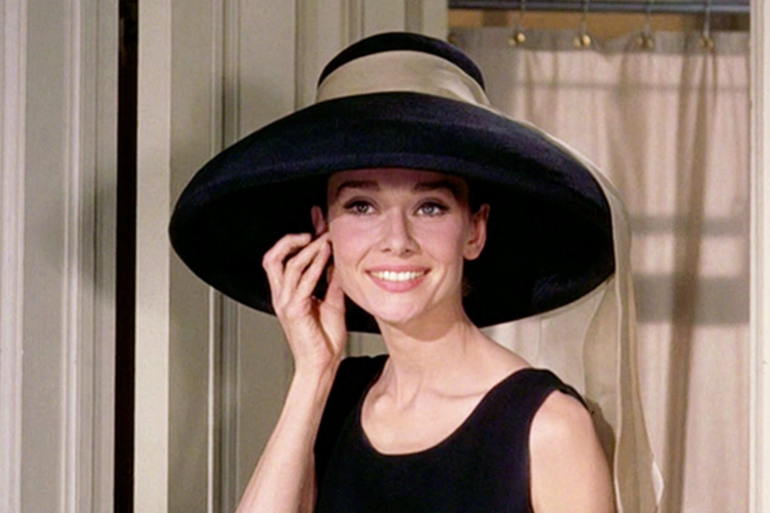 Audrey Hepburn hatalmas fekete kalapban, fülét fogja