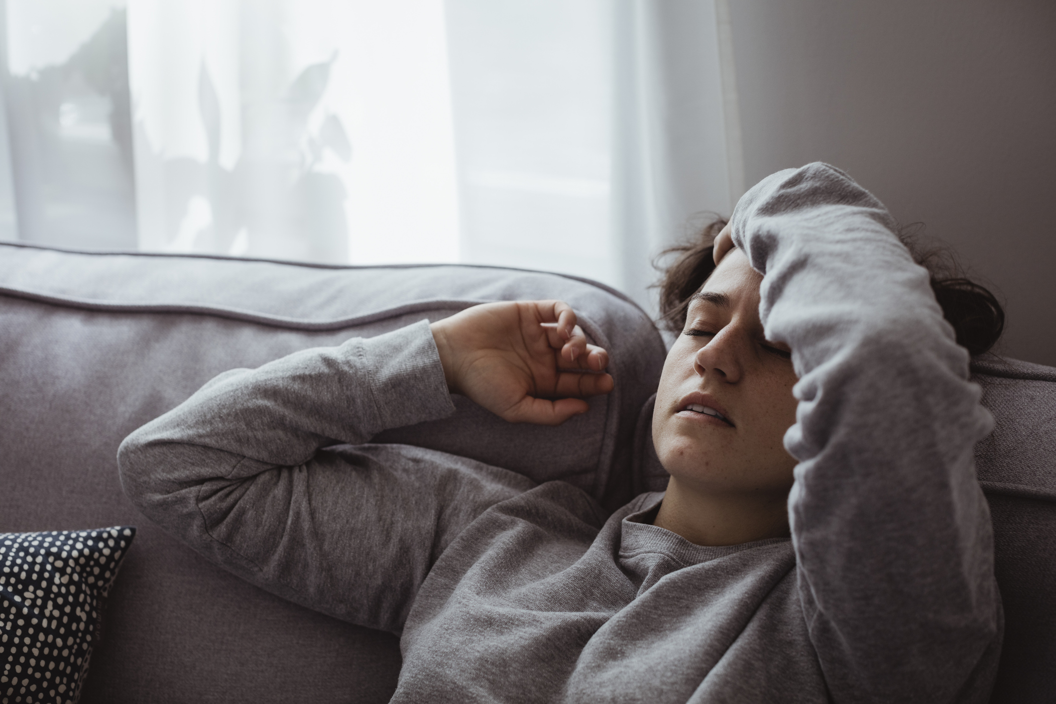 Fiatal lány fejfájással fekszik a kanapén