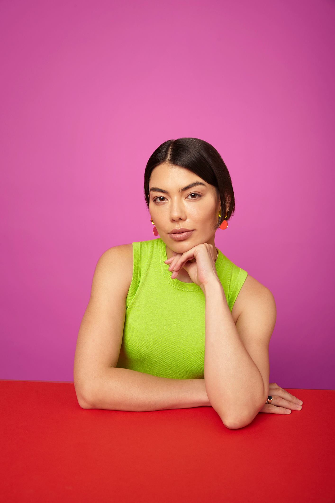 mondatok-nok-tisztelet-ferfiak | Marie Claire Egy gyönyörű nő könyököl az asztalon és magabiztosan néz, mögötte rózsaszín fal