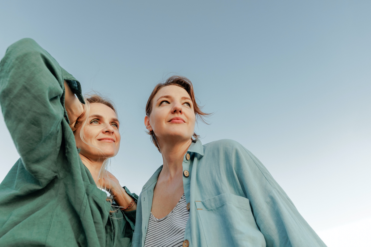 Két középkorú nő portréja közelről, háttérben kék ég.