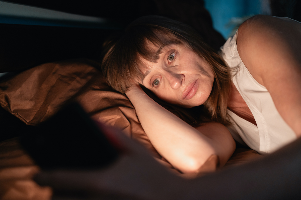 álmos nő nem tud aludni, az ágyban fekve mobiltelefont néz, ennek fénye világítja meg az arcát