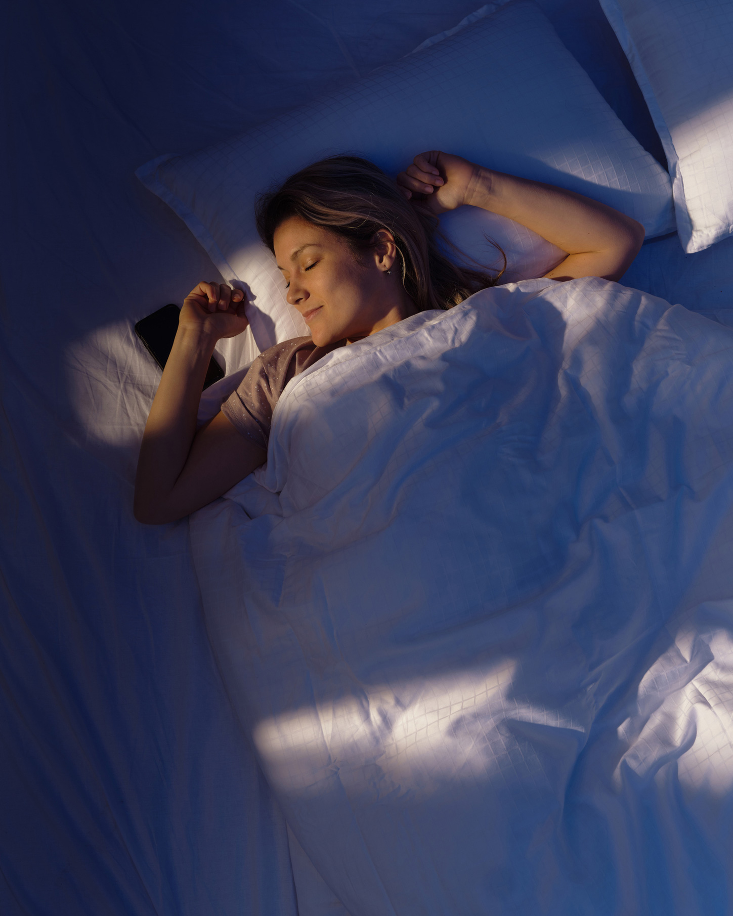 Magas szögből készült kép egy nyugodt, mosolygós nőről, aki valami szépről álmodik éjszaka.