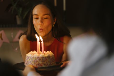 Nő elfújja a szülinapi tortáján a gyertyákat.