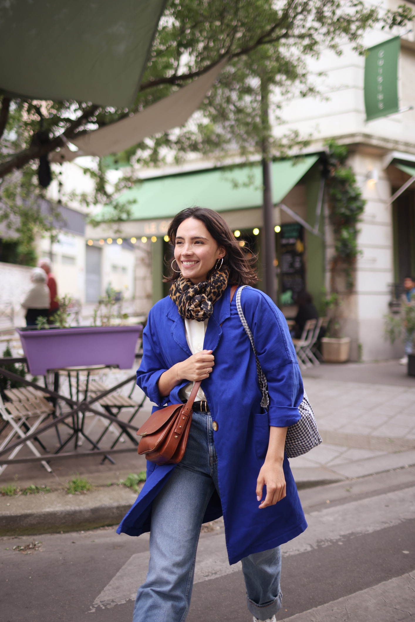 Fiatal kék kabátos nő sétál mosolyogva az utcán