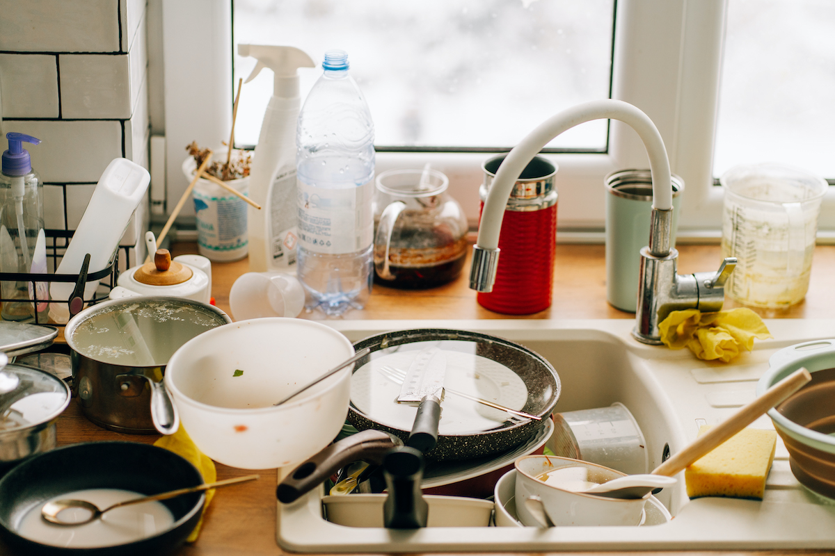 konyhaablak előtt mosogató, amelyből dől ki a mosatlan edény
