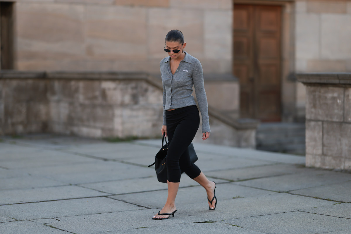 street style: napszemüveges nő fekete capri leggingsben és szürke kardigánban, a kezében táska