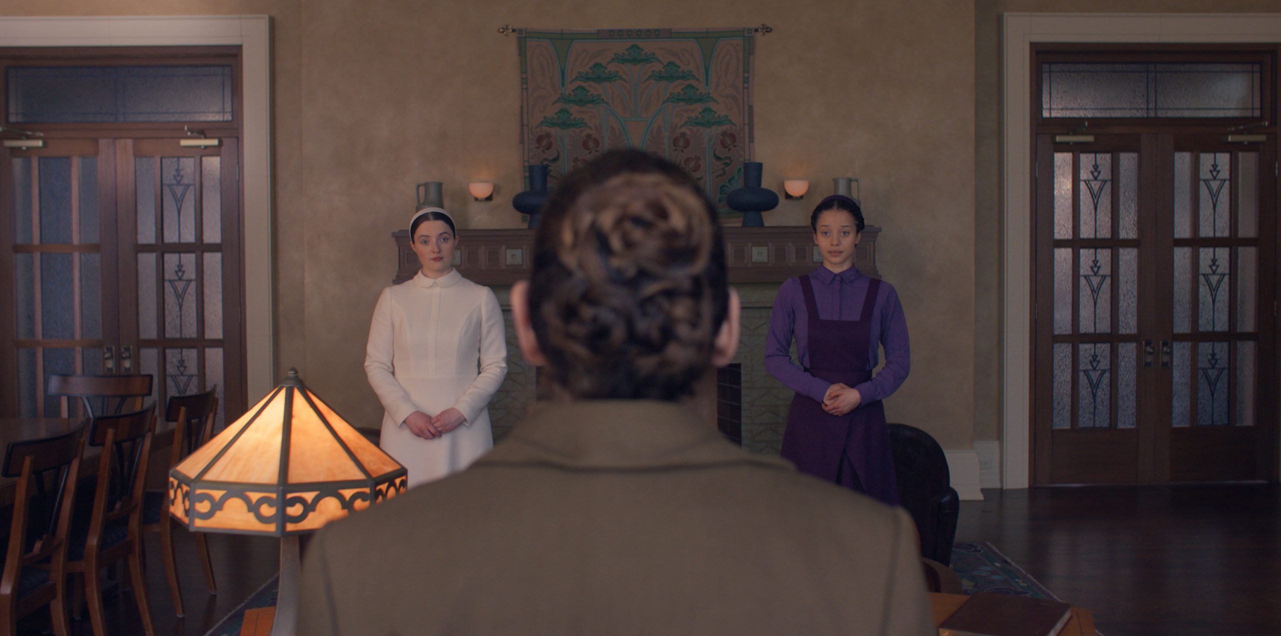 az előtérben háttal egy kontyos nő, vele szemben fiatal lányok: az egyik fehér, a másik lila ruhában.