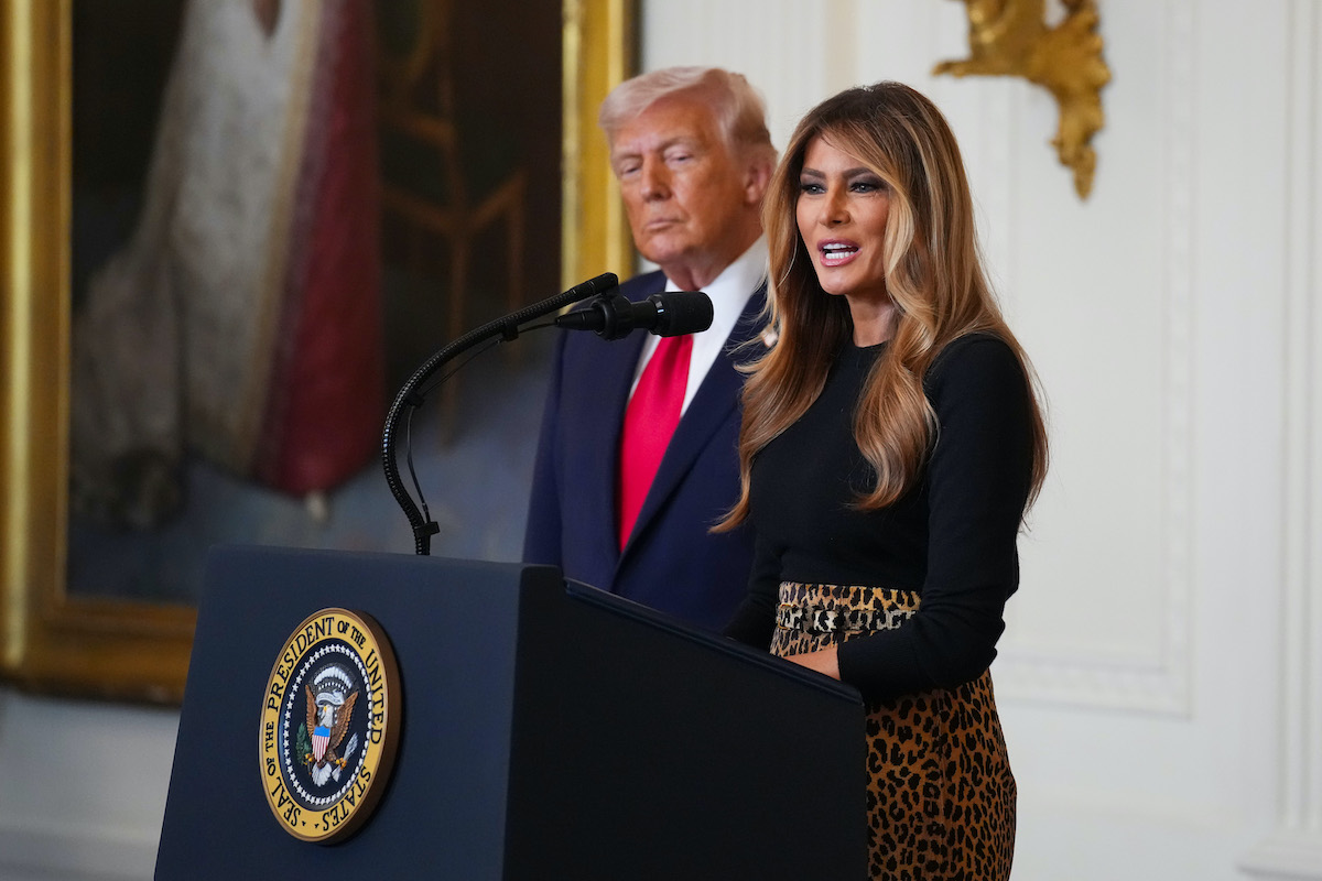 Melania Trump fekete felsőben beszédet mond és mellette Donald Trump piros nyakkendőben