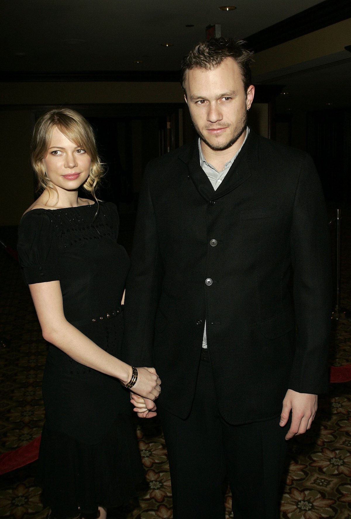 Heath Ledger és Michelle Williams kézen fogva, feketében, sötét háttér előtt állnak
