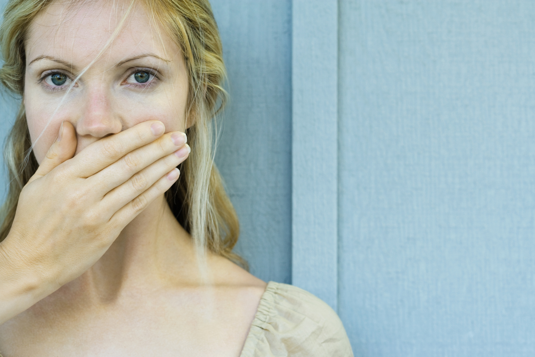 Nő, aki kezével eltakarja a száját, és a kamerába néz