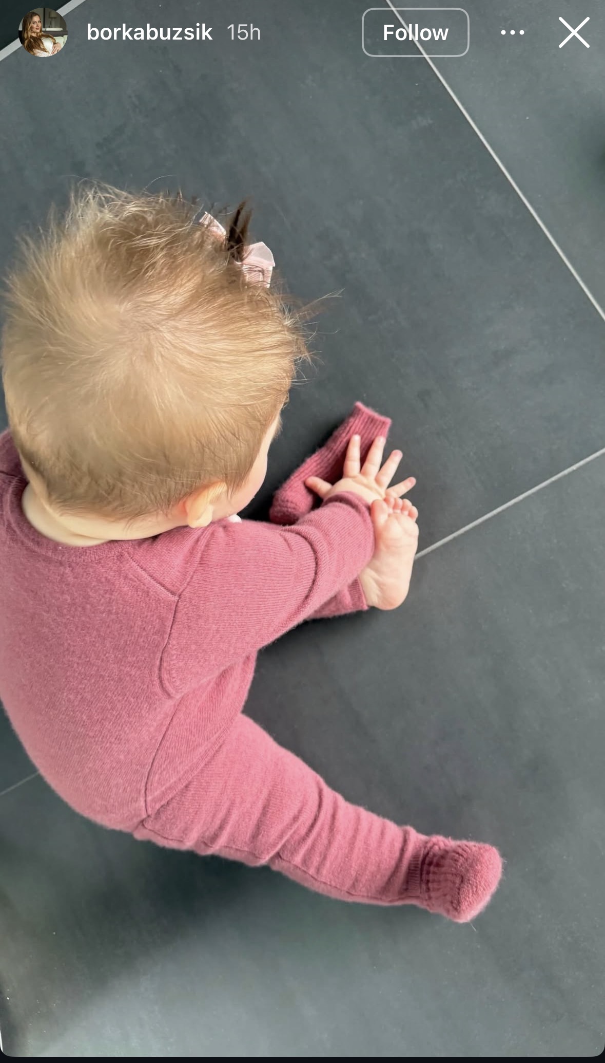 Szoboszlai Dominik kislánya a földön ül rózsaszín kezeslábasban, copffal