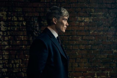 Cillian Murphy fekete téglafal előtt, profilból